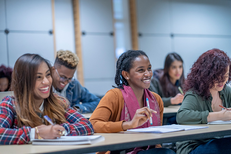 A black female student smiles cheerfully while sitting next to classmates