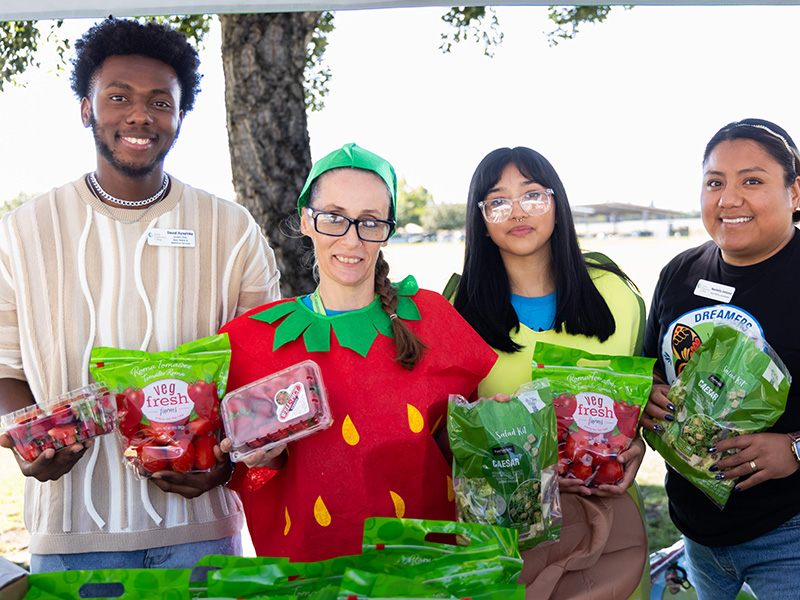 Some people at the farmers market posing with fruits and vegetables while dressed as fruits and vegetables.