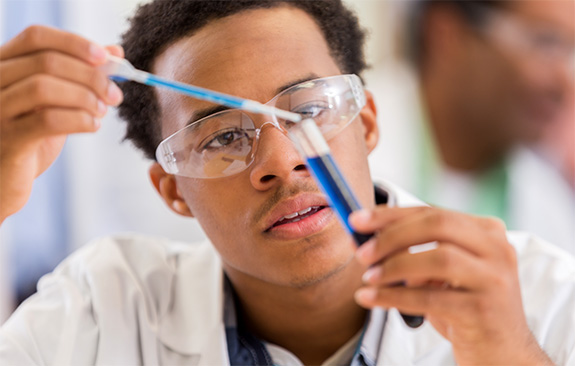 A chemistry student wearing safety goggles and holding a test tube