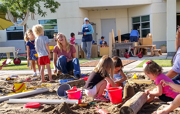 Some kids playing in a big sandbox while adults supervise