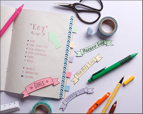 a bullet journal surrounded by stickers, pens and scissors, 