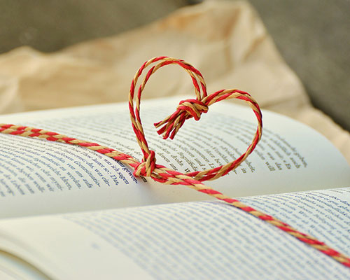 A heart-shaped knot made of red and yellow twine resting on an open book page.