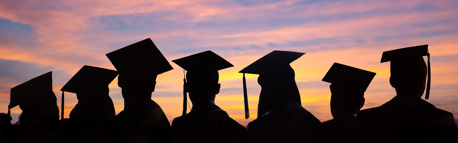 silhouette of students with graduation caps against an orange sunset