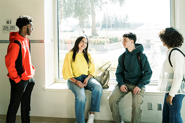 A group of students chat next to a sunny window